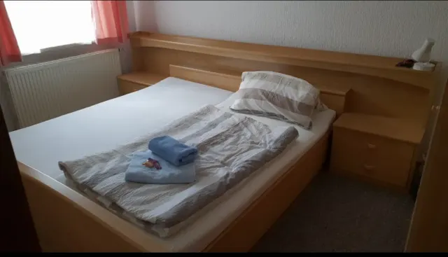 BookNoFees: vakantiehuis in Schönfeld – Slaapkamer met houten bedframe, opgevouwen handdoeken en een raam met roze gordijnen